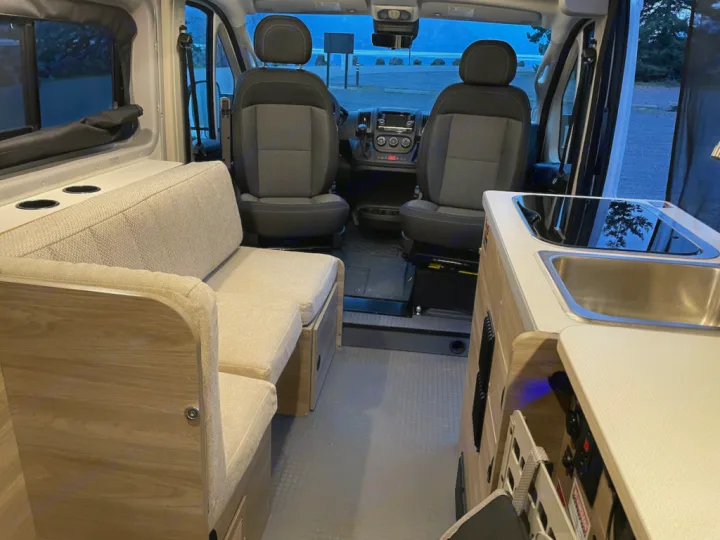 RV rental camper van interior: Features a comfy seating area, a compact kitchen with sink and stovetop, plus front cabin.. Winnebago pocket 2023