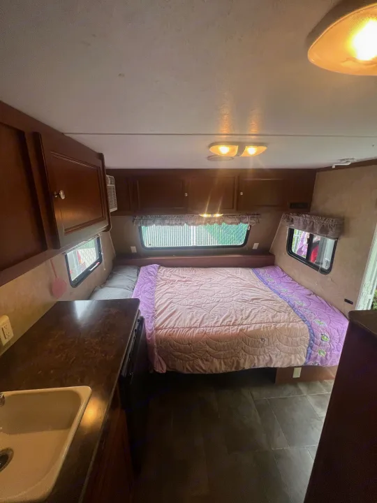 RV rental interior: A compact space featuring a bed with pink and purple bedding, kitchenette, and cabinets.. Dutchmen Coleman Expedition LT 2013