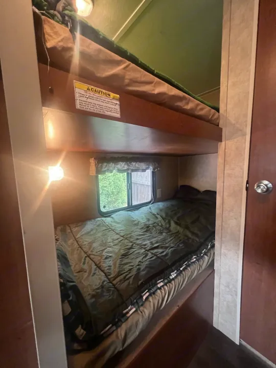 Inside an RV rental: two cozy bunk beds. The lower bunk features a window and light, with a safety warning above.. Dutchmen Coleman Expedition LT 2013