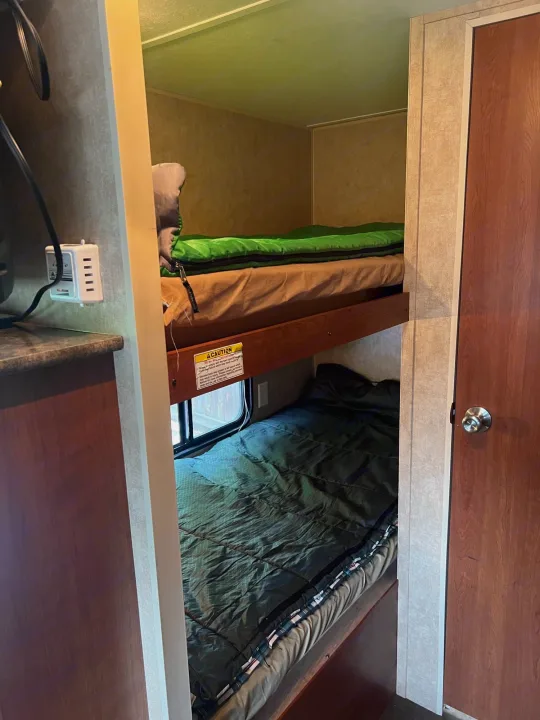 RV rental interior features two bunk beds with green sleeping bags, offering a comfortable sleeping area.. Dutchmen Coleman Expedition LT 2013