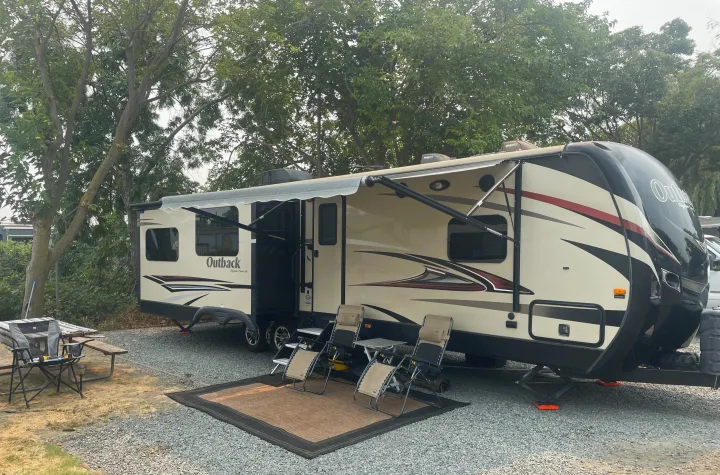 Outback travel trailer RV rental parked at a gravel campsite with its awning extended, outdoor chairs, and a picnic table.. Keystone 316-UL 2014