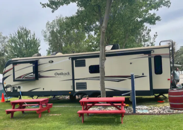 RV rental setup at a campsite with red picnic tables, surrounded by green grass and trees.. Keystone 316-UL 2014