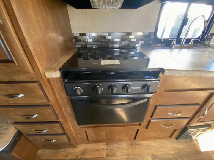 Explore this RV rental kitchen's compact design: black stove, oven, sink, and ample wooden cabinet storage.. Forest River Salem Cruise Lite 2018