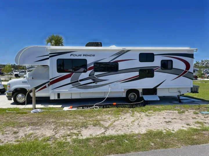 White Four Winds RV rental parked at a sunny campground, connected and ready for travel adventures.. Thor Four Winds 2022