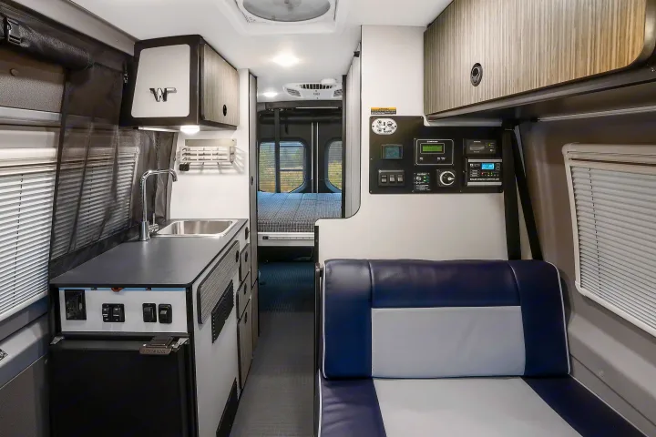 Bright rv rental interior, showing a kitchen counter with sink, tech control panel, seating area, and bed in the rear.. Winnebago Revel 2022