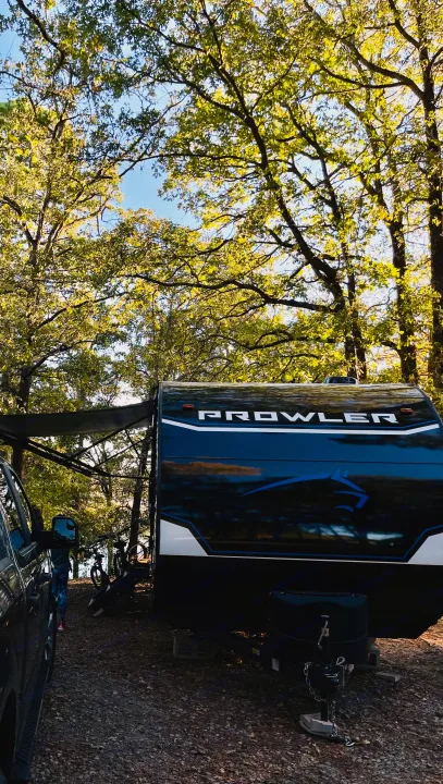 A Prowler RV rental and truck parked under lush green trees by a lake, with bicycles nearby, for an outdoor adventure.. Heartland Prowler 2021