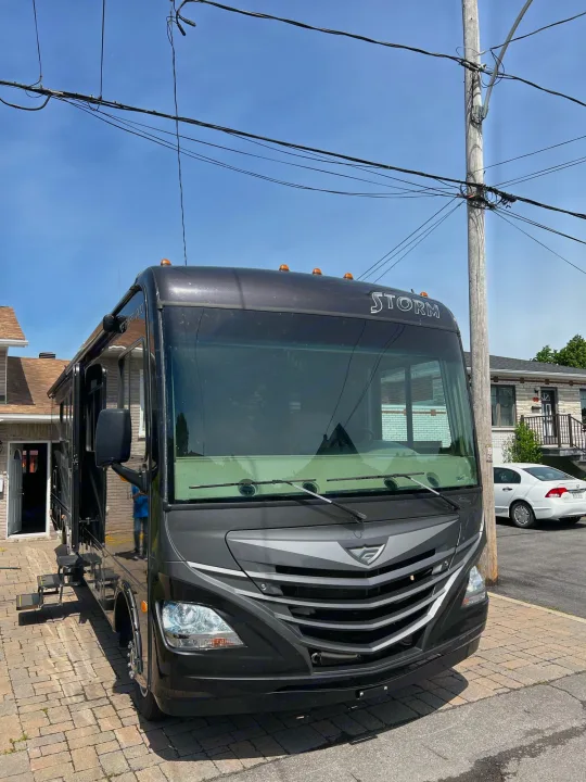 A sleek dark grey Storm RV motorhome, suitable for an RV rental, parked on a brick driveway near houses and power lines.. Fleetwood Other 2015