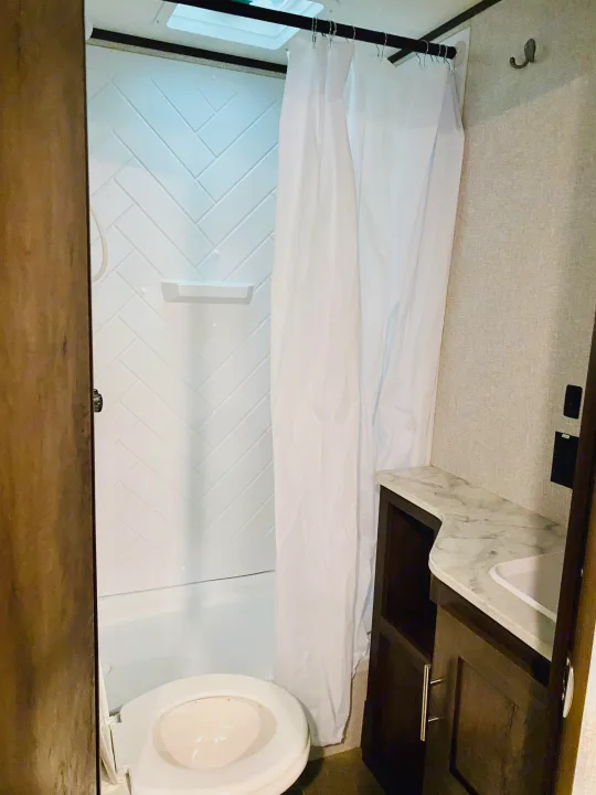 Inside this RV rental's bathroom: a compact white shower, toilet, and modern vanity with a marble-look counter.. Coleman Lantern 2021