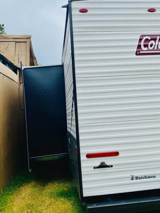 Side view of a Coleman Dutchmen RV rental with its extended black slide-out, parked by a wooden fence. Ready for adventure!. Coleman Lantern 2021