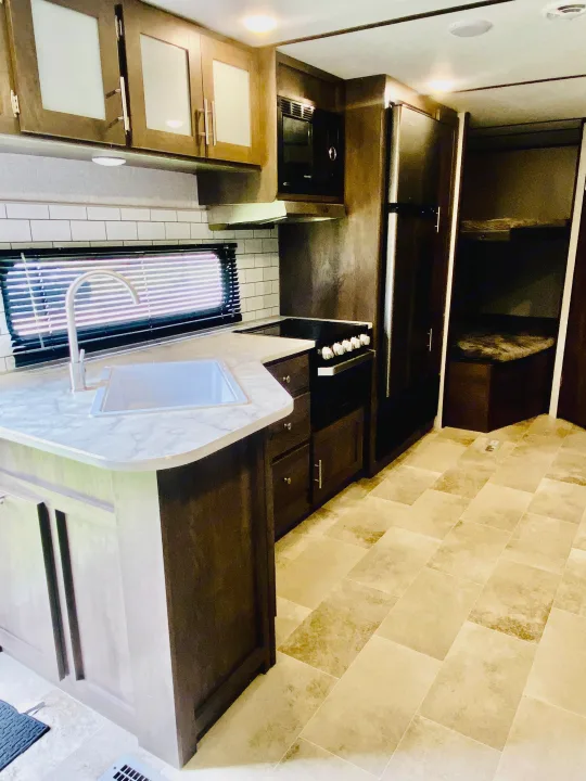 Modern RV rental interior: kitchen with sink, microwave, stove, fridge, subway tile, and bunk beds visible.. Coleman Lantern 2021