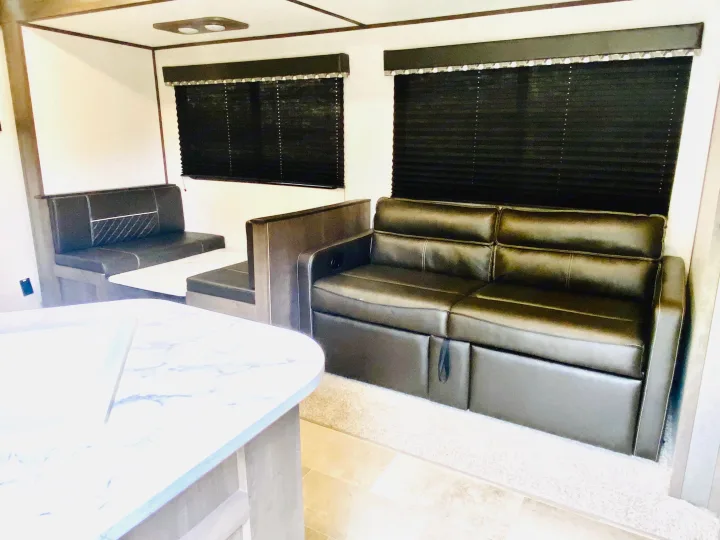 RV rental: Inside, a comfortable living space with a black sofa, dining booth, white counter, and dark privacy blinds.. Coleman Lantern 2021