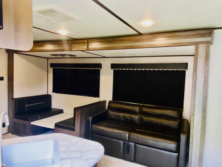 Comfy RV rental interior with a dark dinette booth, plush sofa, and black-out window blinds. Kitchen counter visible.. Coleman Lantern 2021