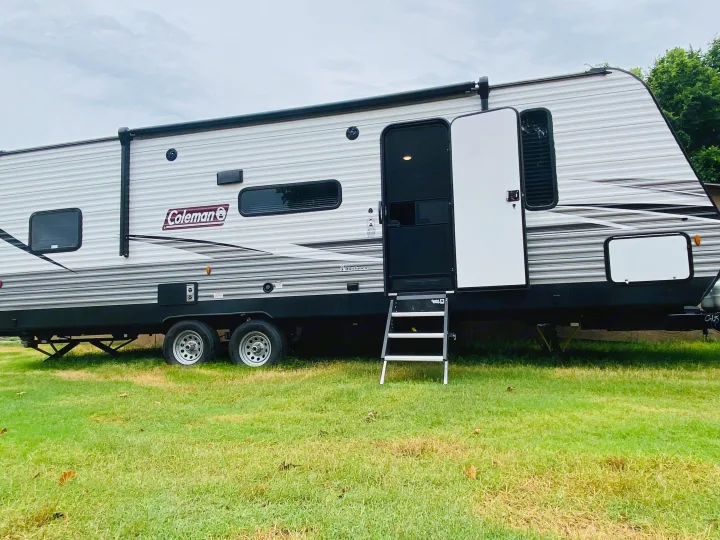 This gray Coleman RV rental travel trailer with an open door and steps on a grassy campsite is ready for adventure.. Coleman Lantern 2021
