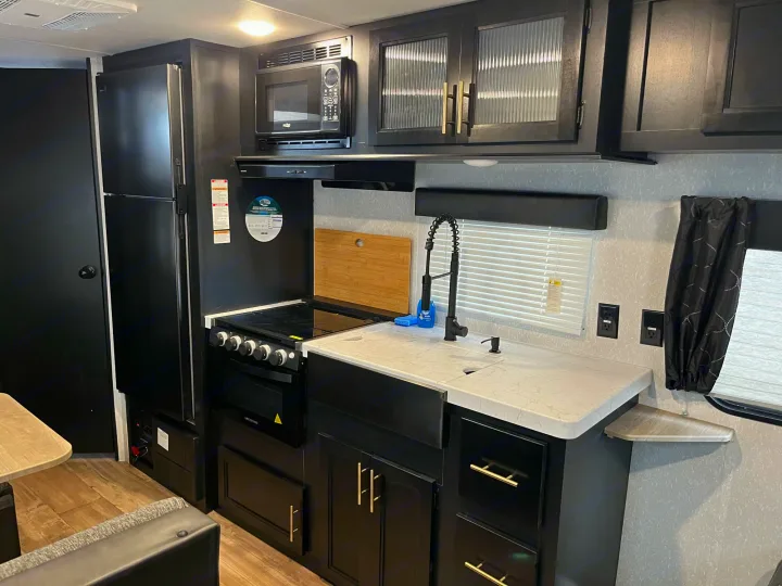 This RV rental boasts a modern kitchen with black cabinets, light counters, a stove, microwave, and integrated sink.. Forest River Cherokee Grey Wolf Special Edition 2022