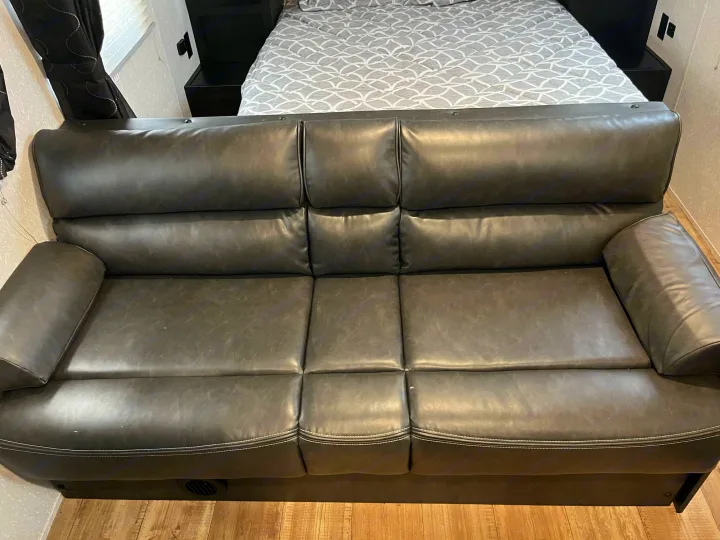 Inside an RV rental: a dark gray sofa with white stitching offers seating, with a bed visible in the background.. Forest River Cherokee Grey Wolf Special Edition 2022