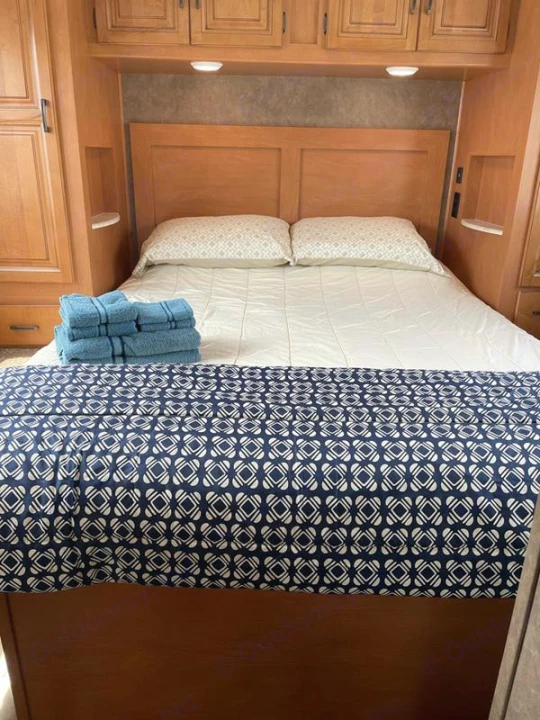 Relax in this cozy RV rental bedroom. Features a comfortable bed with pillows, a patterned blanket, and fresh blue towels.. Sunseeker 2650 2015
