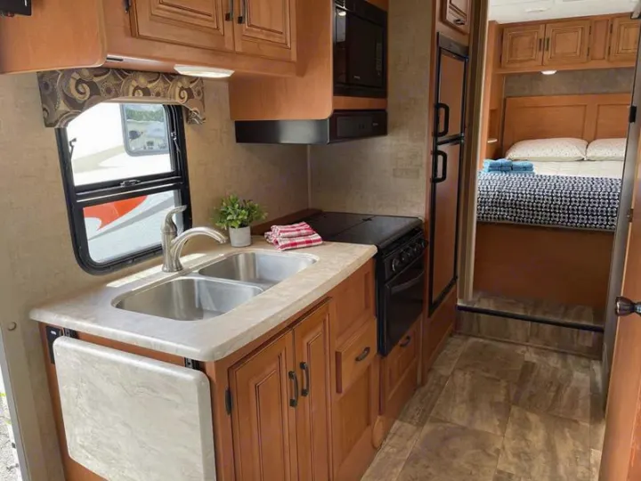 RV rental interior with a well-equipped kitchen (sink, stove, microwave) and a view into the comfortable bedroom area.. Sunseeker 2650 2015