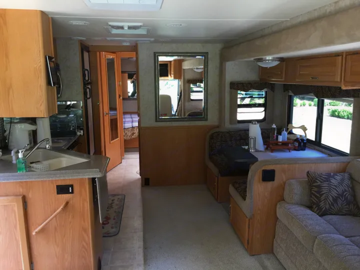 This RV rental's interior features a kitchen, dining booth, living area with couch, and glimpse of the bedroom.. National RV Sea Breeze 2006