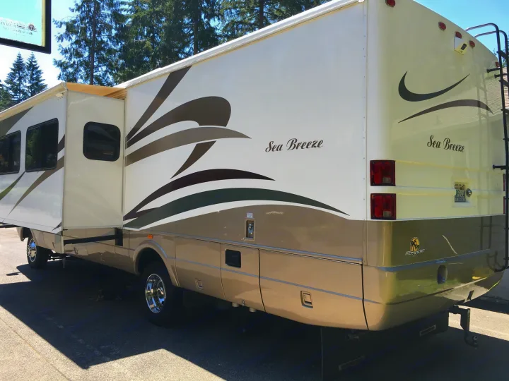 Side view of a white and tan 'Sea Breeze' RV, with its slide-out extended and a rear ladder, perfect for rv rental.. National RV Sea Breeze 2006