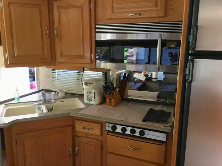 Inside an RV rental, featuring a functional kitchen with light wood cabinets, sink, microwave, stove, and refrigerator.. National RV Sea Breeze 2006