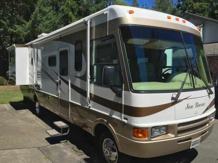A white and gold "Sea Breeze" motorhome parked outdoors with an extended awning and steps. Ideal RV rental for trips.. National RV Sea Breeze 2006