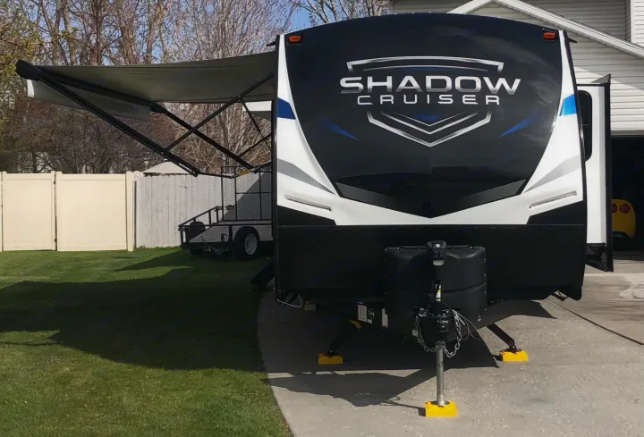 Front view of a black & white Shadow Cruiser travel trailer with awning extended, parked on a driveway. Ideal RV rental.. Cruiser Rv Corp Shadow Cruiser 2021
