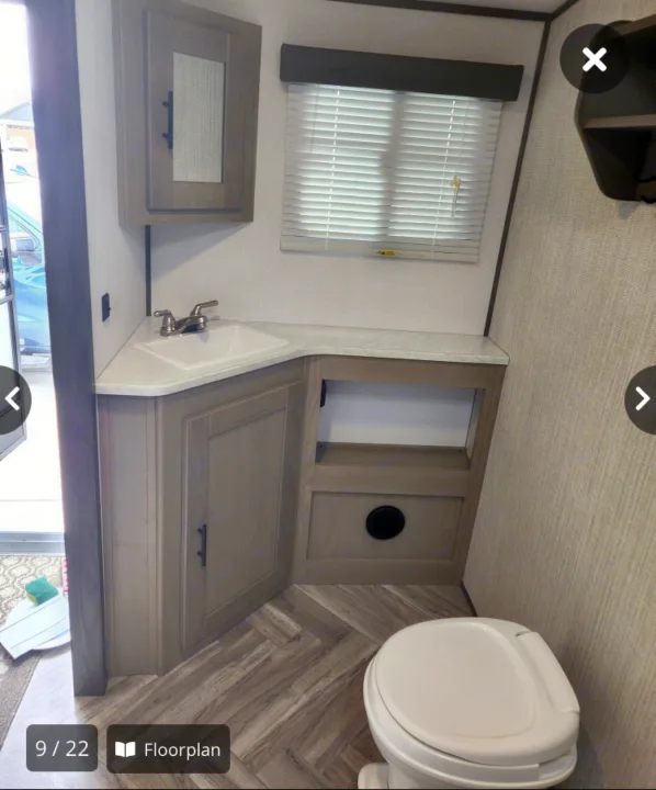 This RV rental bathroom features a corner sink, light wood vanity & cabinet, window with blinds, and toilet. Herringbone floor.. Cruiser Rv Corp Shadow Cruiser 2021