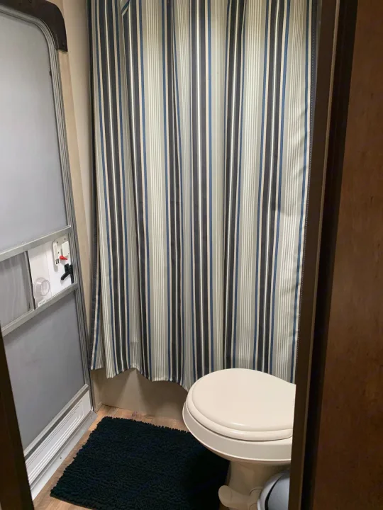 Explore this RV rental's compact bathroom, featuring a shower, toilet, and stylish striped curtain.. Forest River Wildwood X-Lite 2016