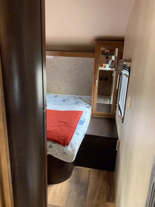 Step inside this RV rental bedroom: bed with floral sheet, orange blanket, mirrored cabinet, and window view.. Forest River Wildwood X-Lite 2016