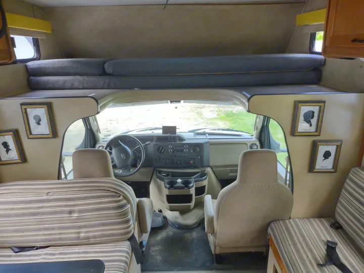 View of an RV rental interior with cockpit, overhead bunk, and striped living area seating.. Thor Four Winds 2013