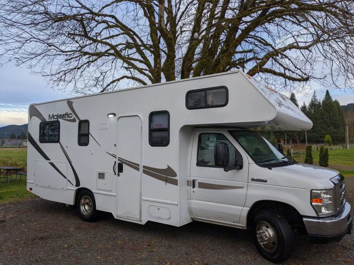 White Majestic Class C RV rental parked on gravel, surrounded by trees and distant hills, ready for adventure.. Thor Four Winds 2013