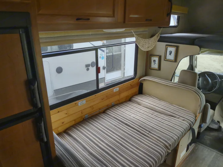 Interior of an RV rental: striped bed/seating, wood details, large window, and cabinets for a cozy travel space.. Thor Four Winds 2013