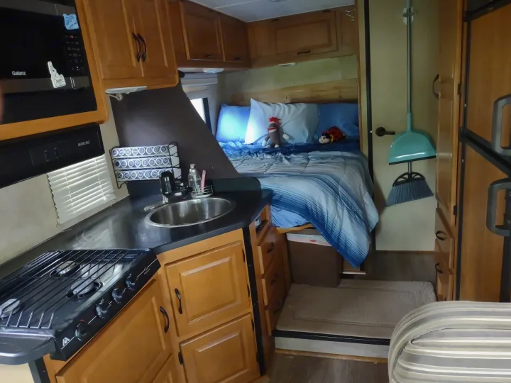 This RV rental offers a compact kitchen with a microwave, stove, and sink, alongside a comfortable bed, designed for travel convenience.. Thor Four Winds 2013