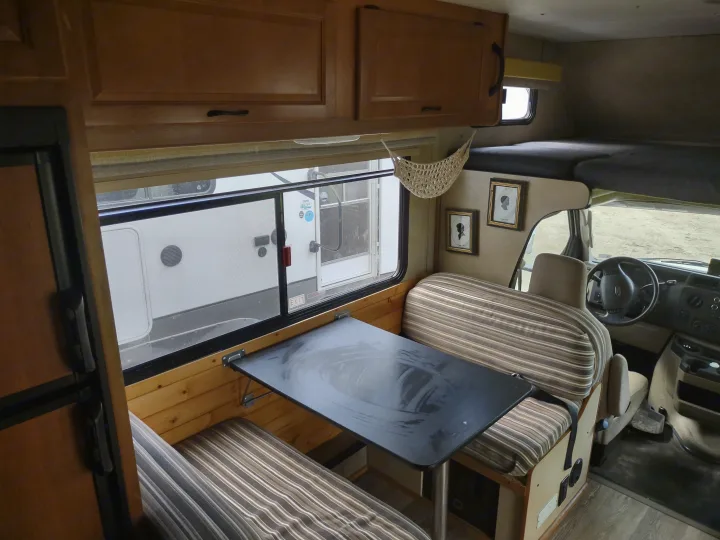 RV rental interior: dinette, galley with fridge, and over-cab bunk visible, ideal for travel adventures.. Thor Four Winds 2013