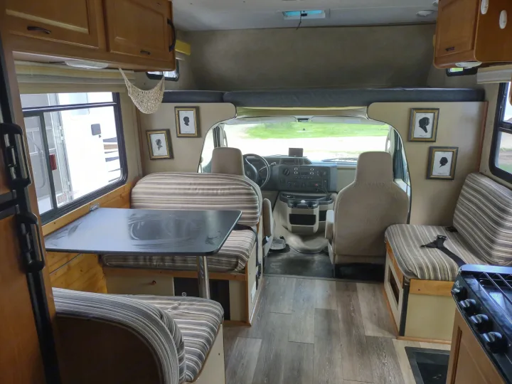 Discover a comfortable RV rental interior with a dinette, kitchen, and front cab. Features wood floors and striped cushions.. Thor Four Winds 2013