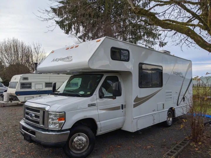 White Majestic Class C RV rental (Ford E-350 motorhome) parked on gravel with bare trees in background.. Thor Four Winds 2013
