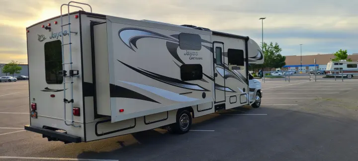 A beige Jayco Greyhawk RV rental, side extended, is parked in a spacious asphalt lot at sunset. Ready for travel!. Jayco Greyhawk 2015