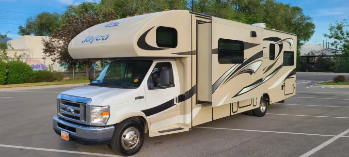Tan Jayco Greyhawk Class C RV rental with black and white graphics, featuring an extended slide-out, parked on asphalt.. Jayco Greyhawk 2015