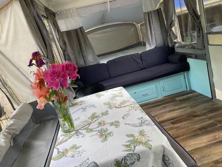Inviting RV rental interior: fresh flowers on a patterned table, a comfy couch, and a cozy pop-out bed area.. Coleman Grand Tour Sun Valley 2002