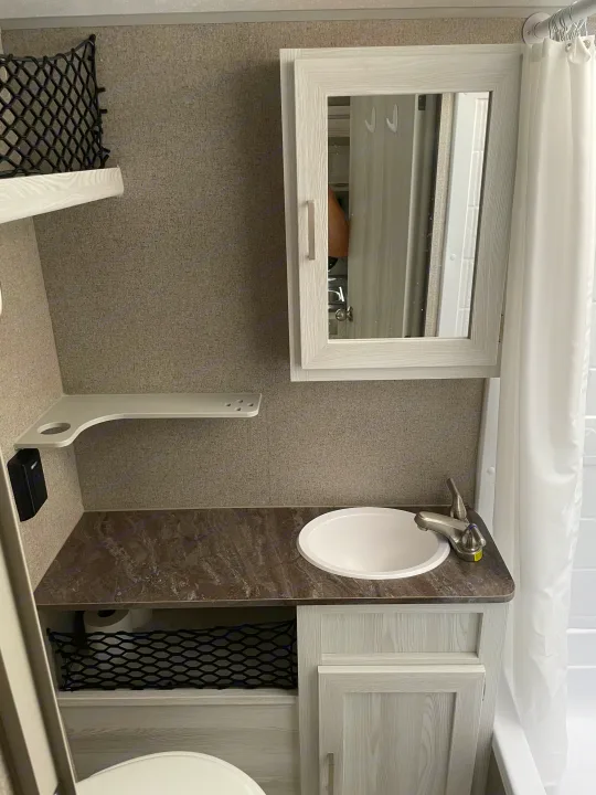 RV rental: Bright, compact bathroom with a white sink, dark counter, light wood mirror, and shower area.. Forest River Flagstaff E-Pro 2020
