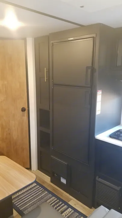 RV rental interior showcasing a modern black Dometic refrigerator, kitchen counter with stovetop, and light wood door. Ideal for compact living.. Keystone RV Springdale 2022