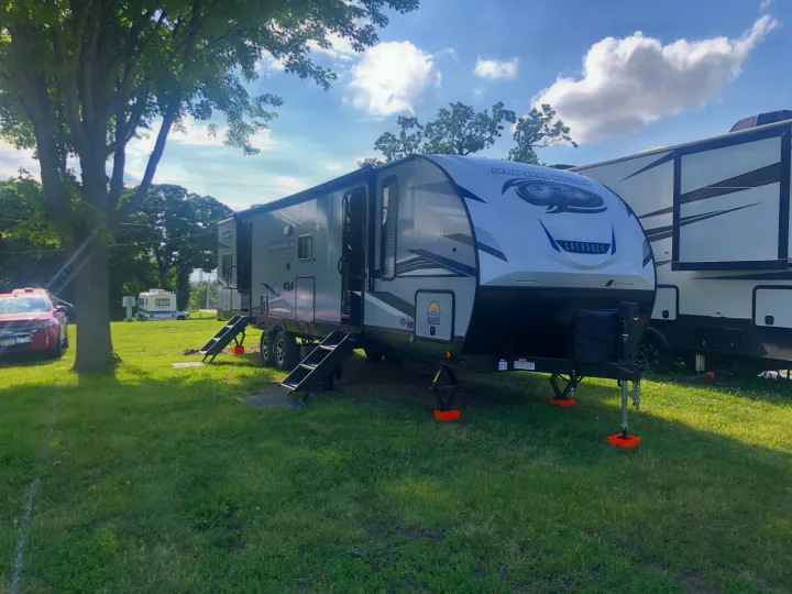 Spacious gray and white RV rental, an Alpha Wolf Cherokee, parked on a sunny green lawn with trees, ready for camping.. Forest River Cherokee Alpha Wolf 2022