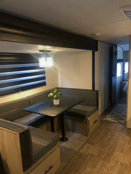 RV rental interior: A U-shaped dinette with table & window blinds. Beyond, a hallway leads to the bedroom. Carpet & wood-look floors.. Forest River Cherokee Alpha Wolf 2022