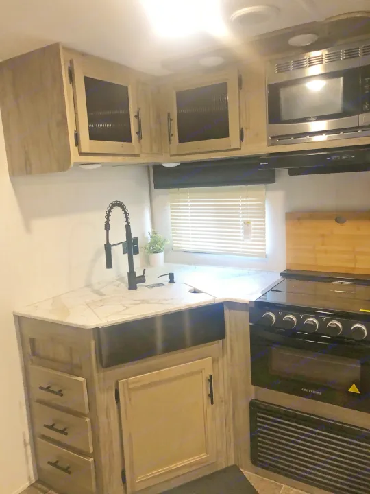 This clean, modern RV rental kitchen features light wood cabinets, white counters, black sink/faucet, microwave & stove.. Forest River Cherokee Alpha Wolf 2022