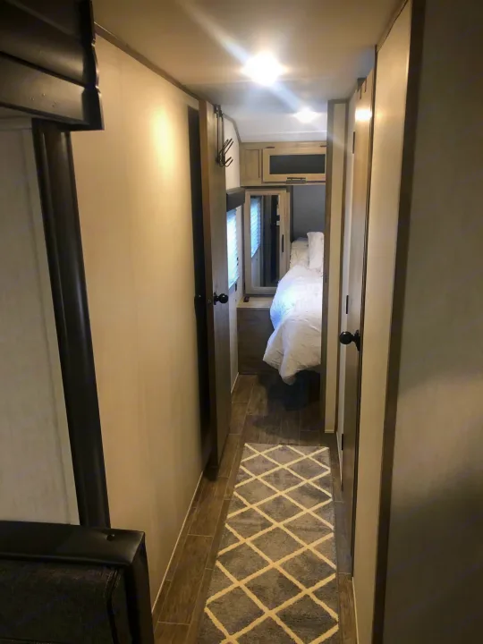 Compact RV rental hallway leading to a cozy bedroom. Features modern decor, wood floors, and a diamond-pattern rug.. Forest River Cherokee Alpha Wolf 2022