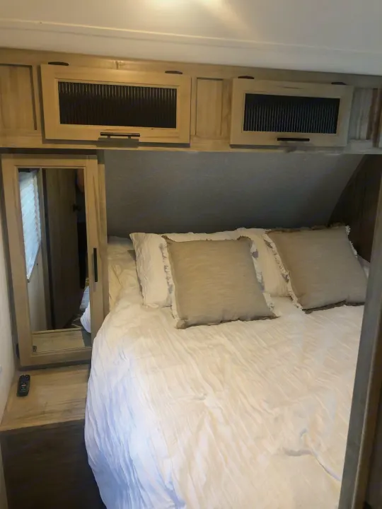 Cozy RV rental bedroom featuring a comfortable bed, stylish pillows, and convenient overhead storage for a perfect getaway.. Forest River Cherokee Alpha Wolf 2022