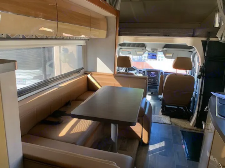 Bright RV rental interior showing dinette, overhead bunk, and cab. Ideal for road trip comfort.. Winnebago Navion 24J 2018