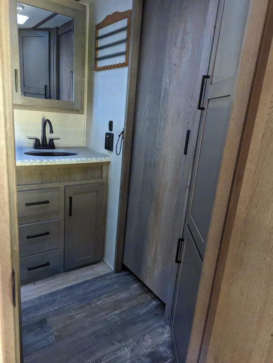 An RV rental bathroom, featuring a modern vanity with a black faucet, sink, mirror, and ample wood-look cabinetry.. Keystone Raptor 2021