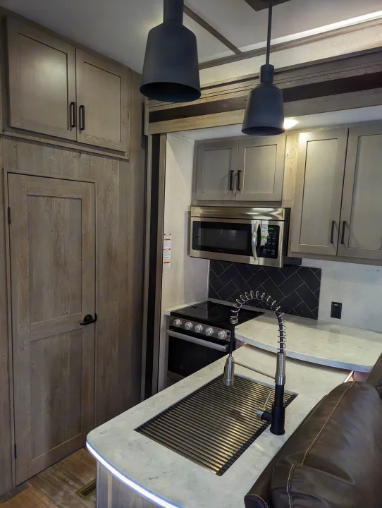 Spacious, modern RV kitchen with light wood cabinets, stainless appliances, sleek counters, and pendant lights, ideal for an rv rental.. Keystone Raptor 2021