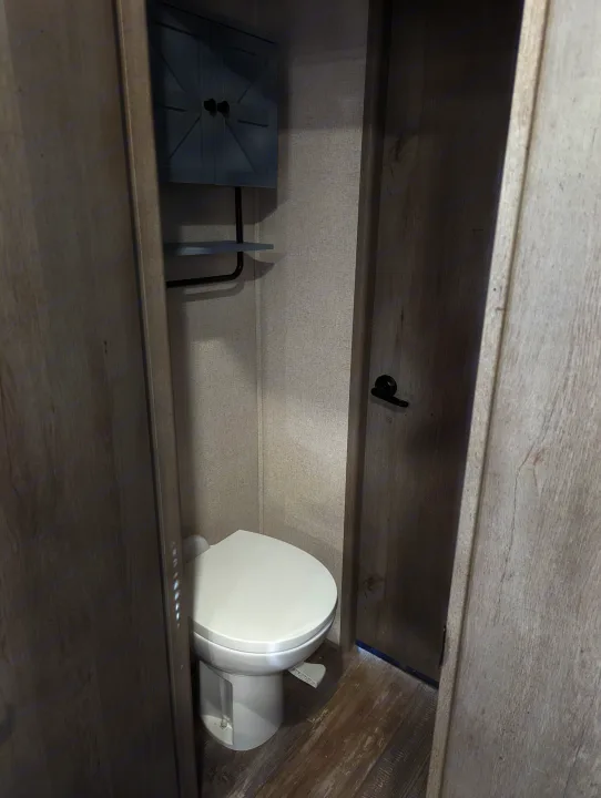 This RV rental bathroom features a compact toilet, overhead cabinet, and wood-look walls. Perfect for mobile living.. Keystone Raptor 2021